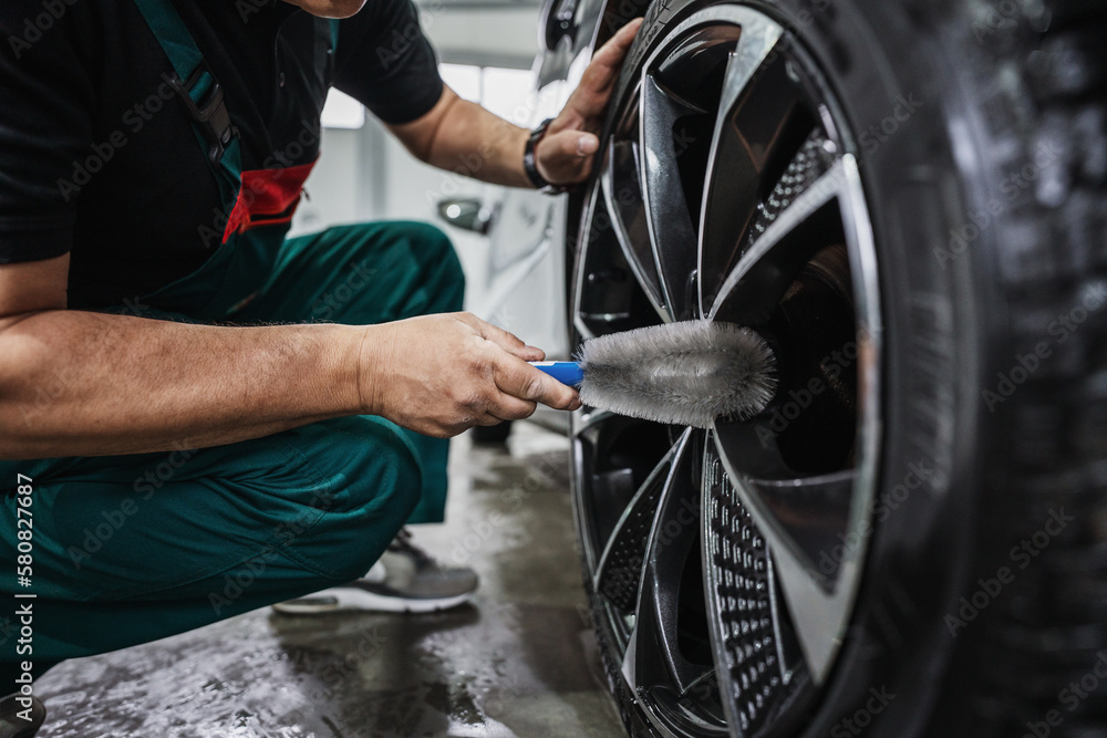 Obraz premium Professional car service worker polishing luxury car rim with microfiber rag or cloth in a car detailing and valeting shop. Ultra wide angle shot.