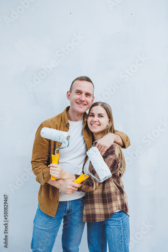 Couple in love, newlyweds in shirts and jeans in an empty room, painting white walls and renovating the interior. A man and a woman moved to a new house. Selective focus