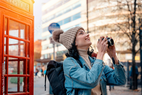 Outdoor portrait of woman using camera against red phonebox in English city