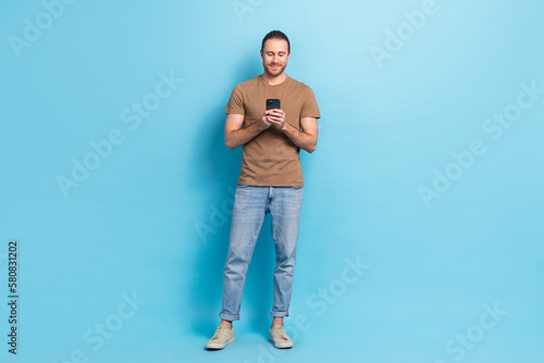 Full length photo of charming sweet man wear beige t-shirt texting modern gadget isolated blue color background