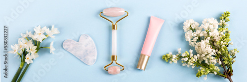 Pink jade roller and gua sha for face massage with cream or gel for the face and flowers daffodils and lilacs. Facial massager tools. Anti age, lifting and toning care. Banner
