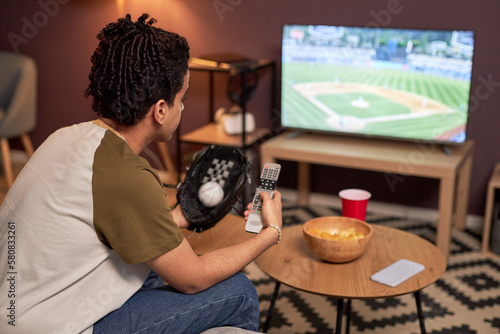 Photography Side view portrait of baseball fan holding TV remote while watching match at hom