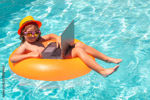 Kids working with laptop on summer vacation holidays. Little freelancer using computer, remote working in swimming pool. Work outside with laptop in pool.