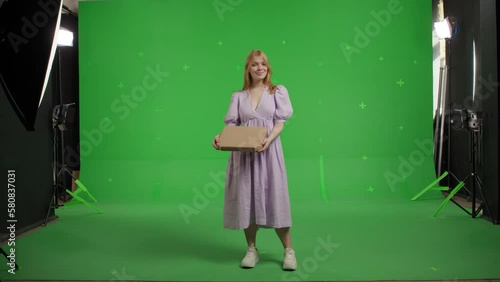 A young attractive red-haired woman holds a box of thin Italian pizza. Smiling girl in a linen dress on a green background photo