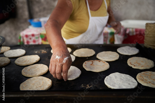 Unrecognizable elderly woman preparing corn tortillas by hand on a griddle in her modest street kitchen