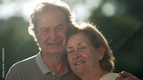 Two joyful seniors smiling at camera. Portrait of older husband and wife embrace close up faces standing outdoors © Marco