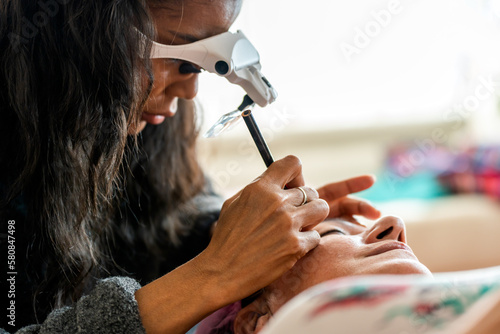 Crop female cosmetologist in magnification goggles making preliminary drawing of eyebrows with pencil during microblading procedure
