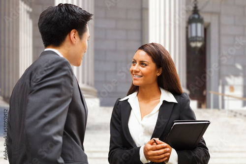 Two well dressed professionals in discussion outdoors in front of a courthouse or government building. Could be lawyers, business people etc.