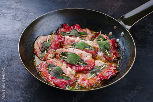 Traditional Italian fried pork saltimbocca alla Romana with Parma ham and sage leaves served as close-up in a classic frying pan photo