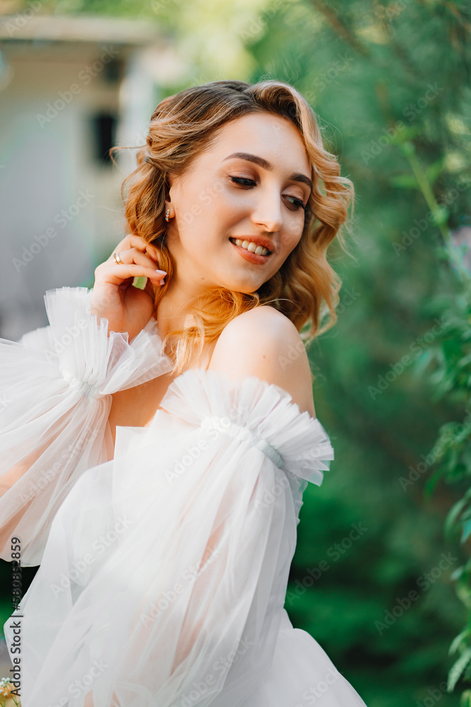 a bride in an open-shouldered dress poses against the backdrop of greenery a bride in an open-shouldered dress poses against the backdrop of greenery