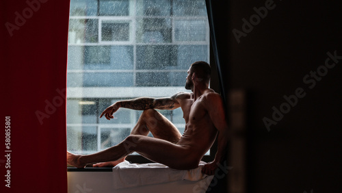 Man with naked body muscular shoulders. Naked man in bed. Muscular sexy male body. Gay sexy model. Muscular sexy man with naked torso near window curtains. Hunk with athletic body. Guy enjoying night. © Volodymyr