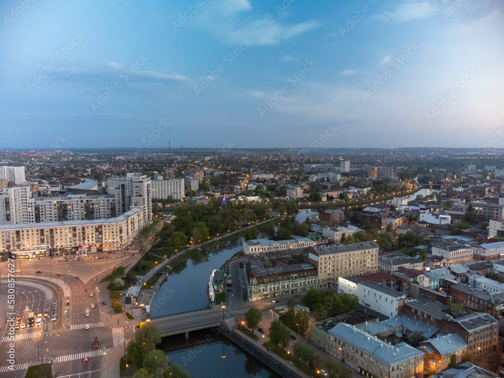City aerial view on bridge across river Lopan, park, embankment and streets in evening lights in spring Kharkiv, Ukraine