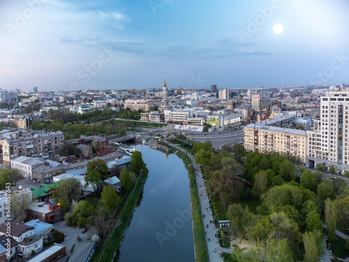 Blue evening city aerial view on river embankment and streets. Skver Strilka park, Dormition Cathedral, square in spring Kharkiv, Ukraine © Kathrine Andi