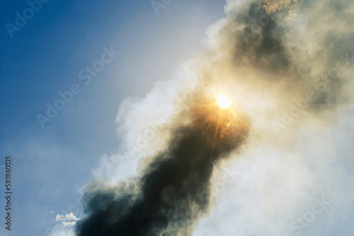 the sun in the sky through a column of smoke from a large fire among forests and dead wood