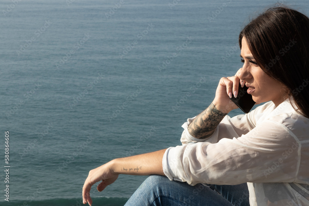 young brunette woman talking on the mobile sitting on the coast