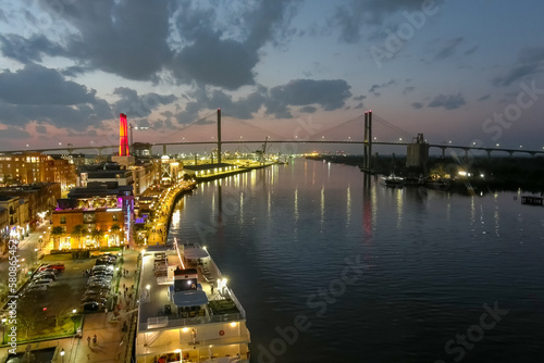 aerial shot of the Savannah River at sunset with the Talmadge Memorial Bridge, ships docked along the banks with restaurants, shops and bars with colorful lights along the Riverwalk in Savannah photo