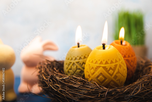 Easter candle eggs in a nest, an Easter bunny and willow branches on a blue table and a blurred light background. Easter holiday concept.Spring willow bouquet.Decor for home and festive steel.