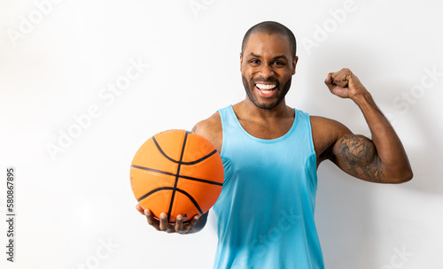 Young handsome dark-skinned sportsman holding basketball over isolated white background with happy expression, positive sign showing joy, winner concept