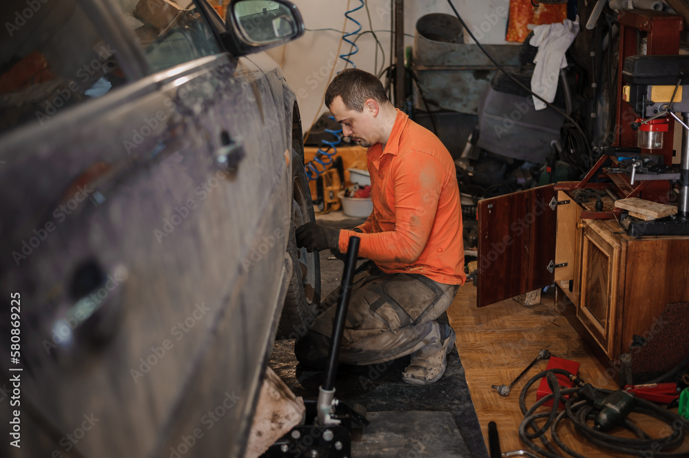 Mechanic man repairs the undercarriage of the car. A man repairs a car in a garage. Car wheel repair