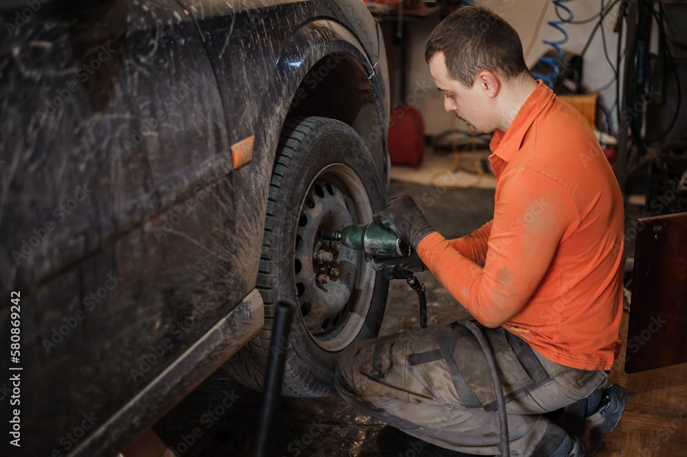 Mechanic man repairs the undercarriage of the car. A man repairs a car in a garage. Car wheel repair