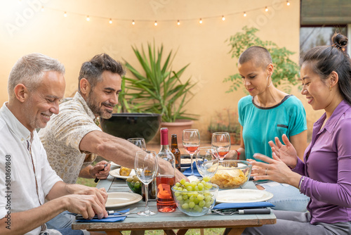 Multiethnic happy friends eating and drinking laughing with beautiful smile around the table. Colorful scene. High quality photo