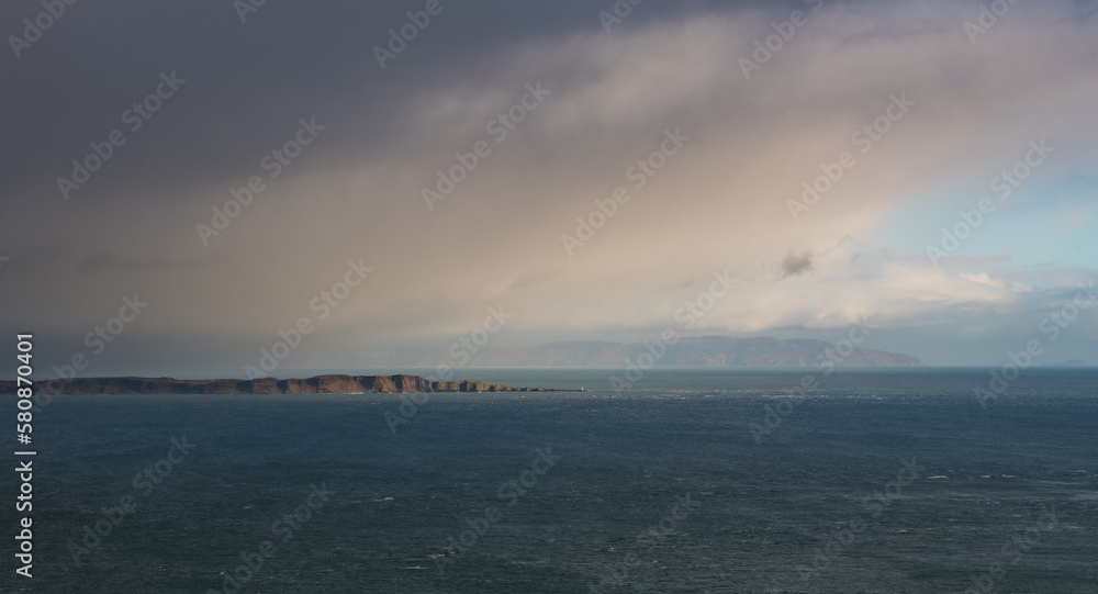 Vast seascape with island illuminated through a break in storm clouds - Northern Ireland
