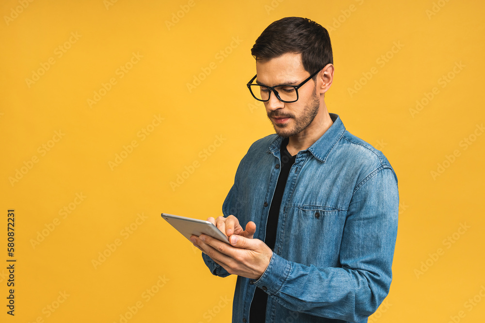 Concentrated on work. Confident young handsome man in casual working on laptop while standing against yellow background. Concentrated on work. Confident young handsome man in casual working on laptop while standing against yellow background.
