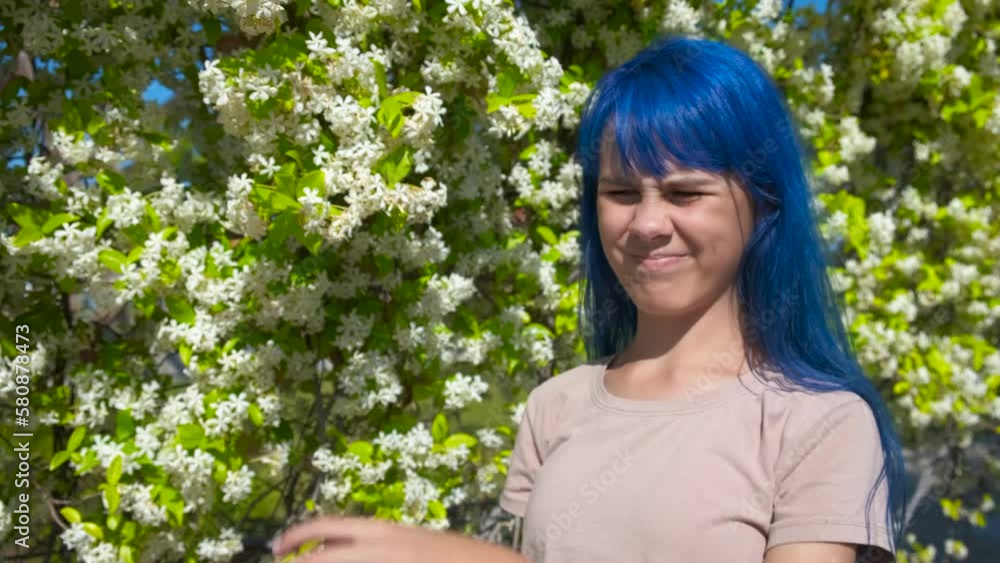 Skin itch, allergy. A teenager with blue hair smells flowers in the park and scratches his hand. Skin itch, allergy. A teenager with blue hair smells flowers in the park and scratches his hand.