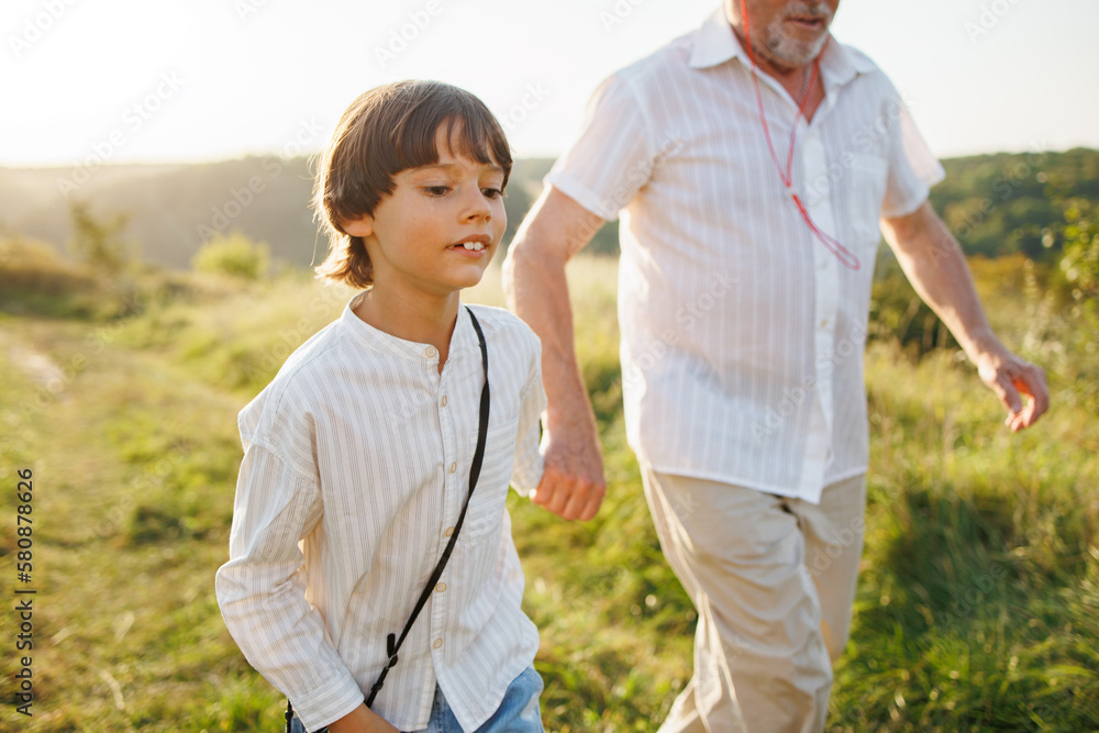 Photo of a little boy with his grandfather walking in a field at summer Photo of a little boy with his grandfather walking in a field at summer