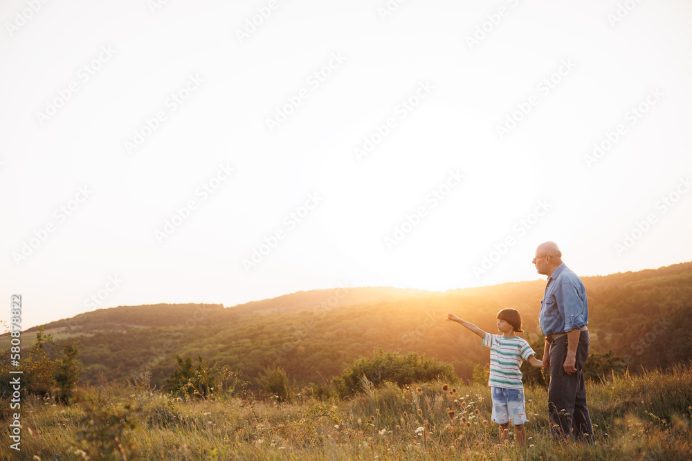 Photo of a little boy with his grandfather walking in a field at summer Photo of a little boy with his grandfather walking in a field at summer