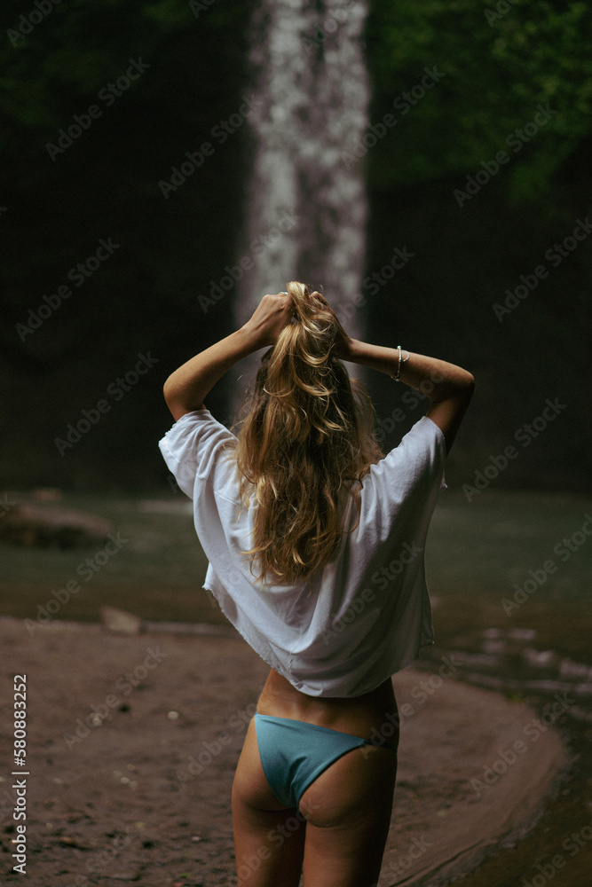 Naklejka premium Woman tourist at a waterfall in the tropical jungle, Bali.