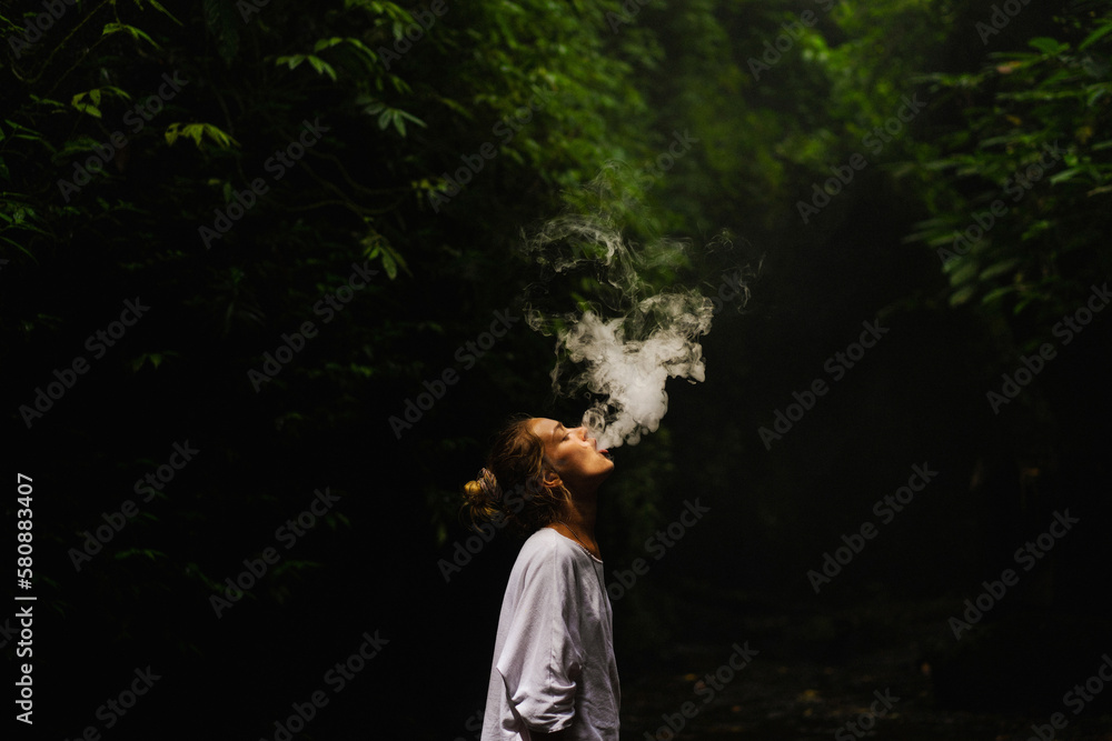 Naklejka premium Young woman smokes a vape in the jungle on a tropical island, Bali.