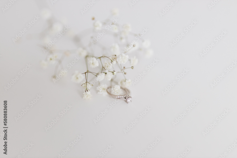 White gypsophila flowers on a white background and engagement ring with a diamond. Surprise for loved one. Gift for Valentine's Day, Mother's Day, International Women's Day. Original marriage proposal White gypsophila flowers on a white background and engagement ring with a diamond. Surprise for loved one. Gift for Valentine's Day, Mother's Day, International Women's Day. Original marriage proposal
