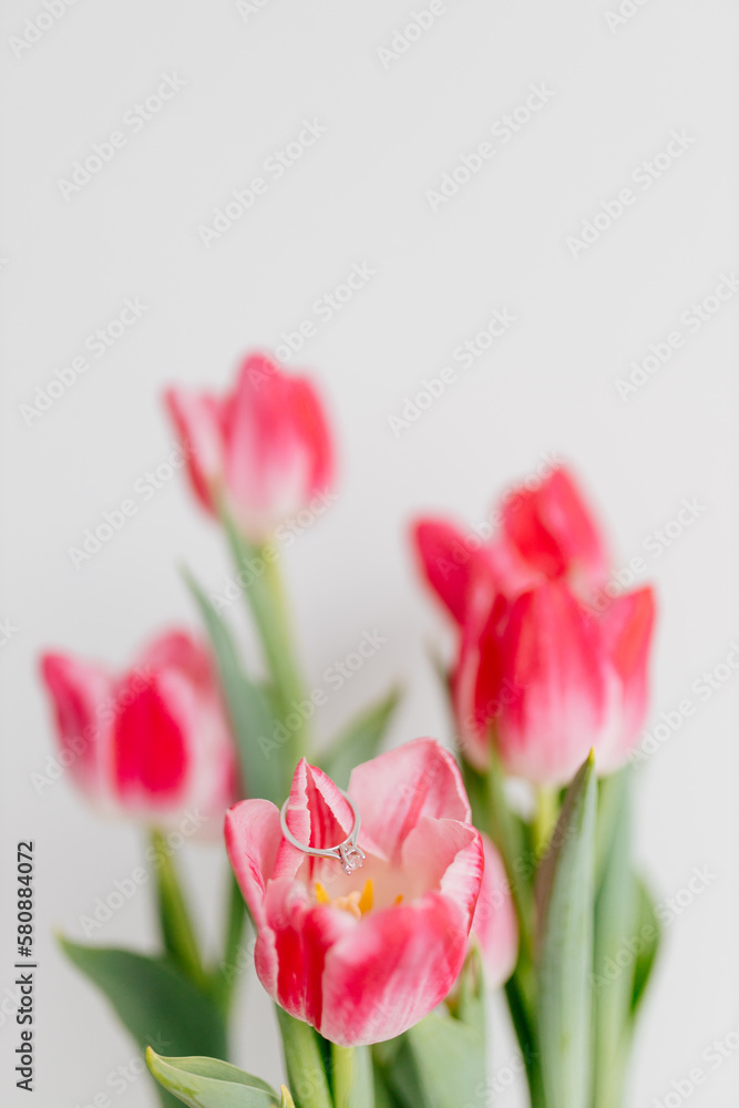 Fototapeta premium Pink tulips and engagement rings with diamonds on white background. Background for Valentine's Day. Gift for Mother's Day, international Women's Day, March 8th. Spring Mock ups. Space for text