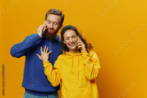 Woman and man cheerful couple with phones in hand talking on cell phone crooked smile cheerful, on yellow background. The concept of real family relationships, talking on the phone, work online.