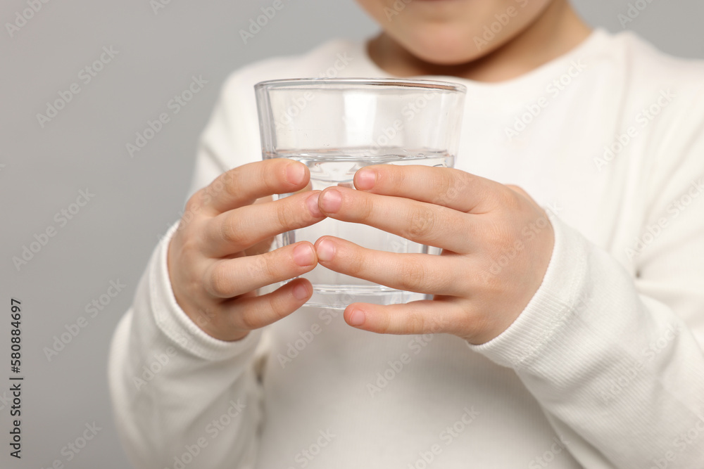 Little girl holding glass of fresh water on light grey background, closeup Little girl holding glass of fresh water on light grey background, closeup
