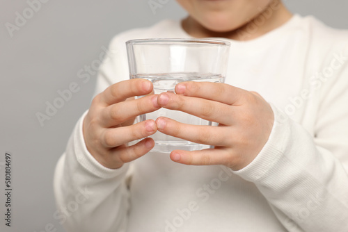 Little girl holding glass of fresh water on light grey background, closeup