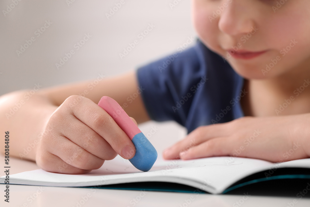 Little boy erasing mistake in his notebook at white desk, closeup Little boy erasing mistake in his notebook at white desk, closeup