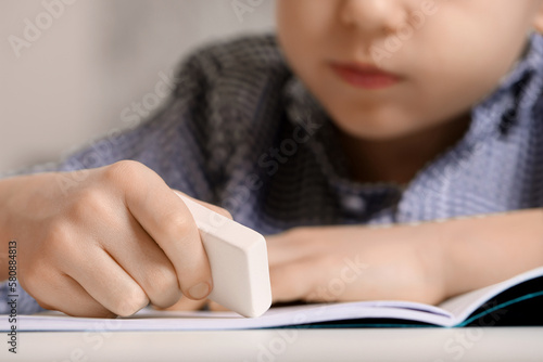 Little boy erasing mistake in his notebook at white desk, closeup