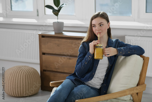 Beautiful young woman drinking delicious smoothie at home. Space for text
