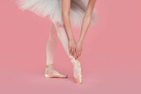 Young ballerina in pointe shoes practicing dance moves on pink background, closeup
