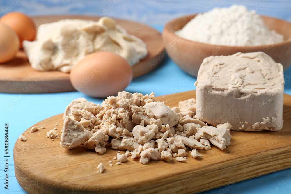 Fototapeta premium Pieces of compressed yeast, eggs and flour on light blue table, closeup