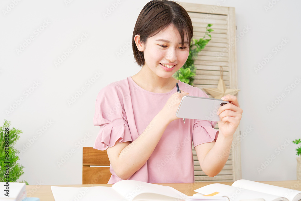 家でスマホで学習アプリを使って勉強する若い女性