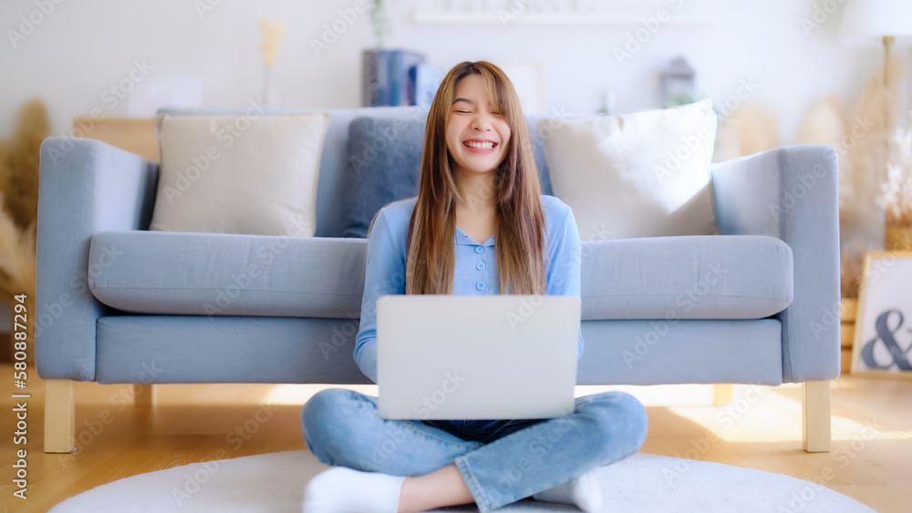 Young asian woman in good spirits working on laptop at home while sitting on the floor close to the couch Young asian woman in good spirits working on laptop at home while sitting on the floor close to the couch