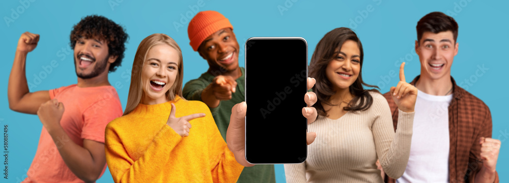 Obraz premium Glad excited millennial multiethnic people show smartphone with blank screen make victory and success gesture