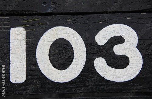 黒い板に白いペンキで書かれた数字「１０３」