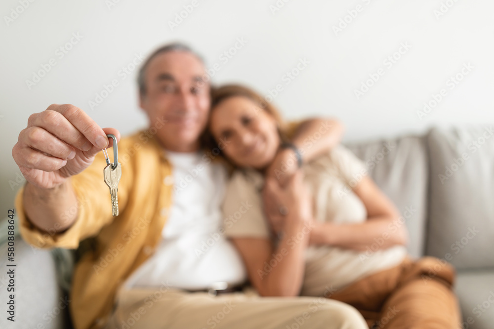 Real estate concept. Senior couple holding home keys, embracing, celebrating buying property, selective focus Real estate concept. Senior couple holding home keys, embracing, celebrating buying property, selective focus