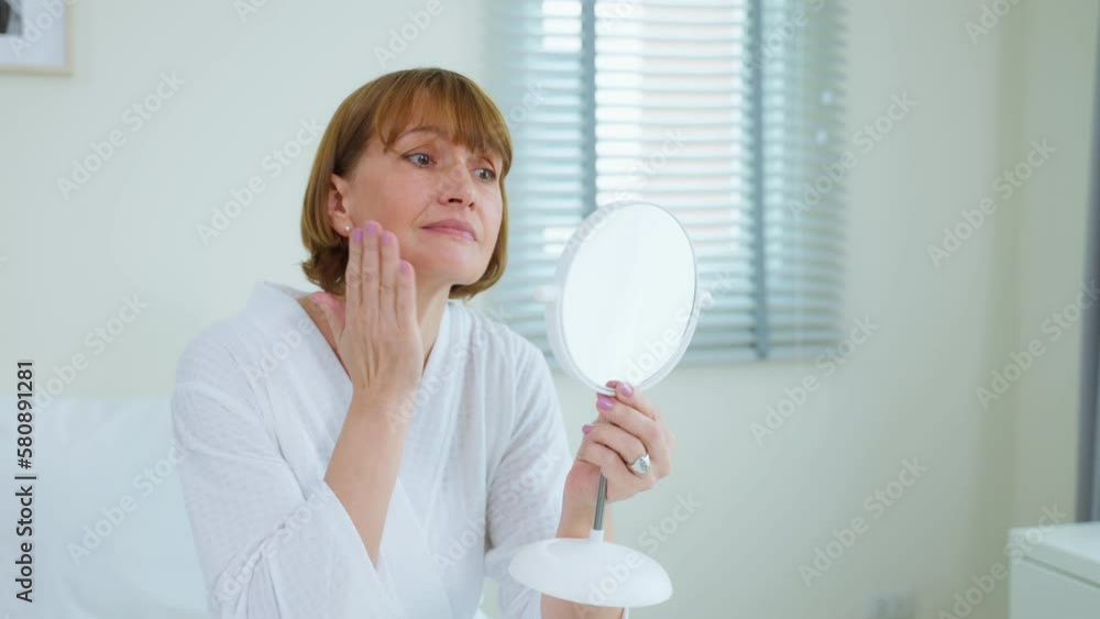 Caucasian senior woman looking at mirror after apply lotion on face. Caucasian senior woman looking at mirror after apply lotion on face.