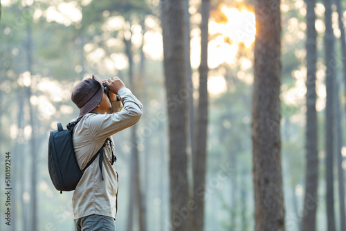 Bird watcher is looking through binoculars while exploring in the pine forest for surveying and discovering the rare biological diversity and ecologist on the field study concept