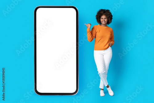 Pretty black young woman pointing at huge cell phone, mockup